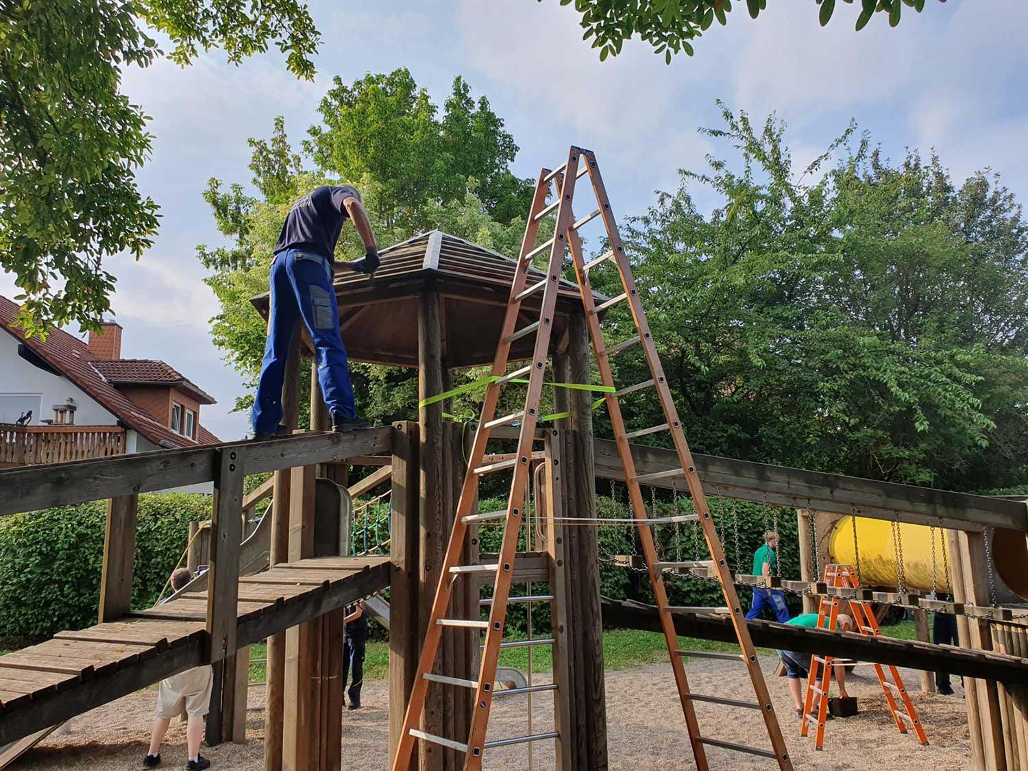 Mann klettert auf das große Klettergerüst und streicht das Dach.