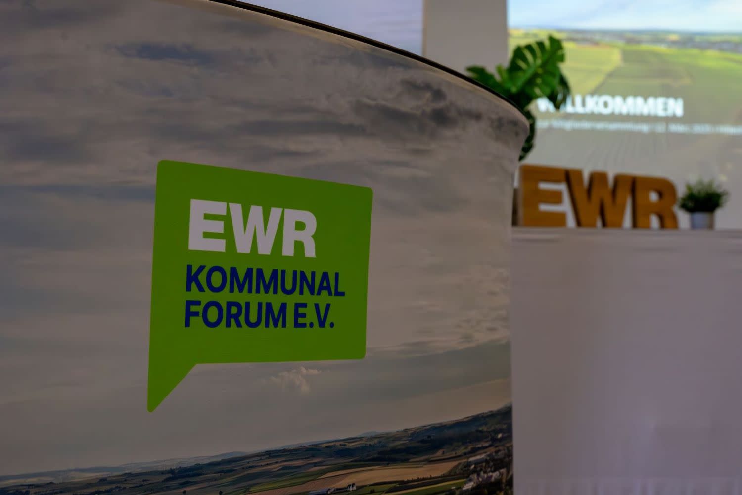 Das Logo des EWR-Kommunalforums e.V. wurde fotografiert. Im Hintergrund ist eine Präsentation der EWR AG zu sehen