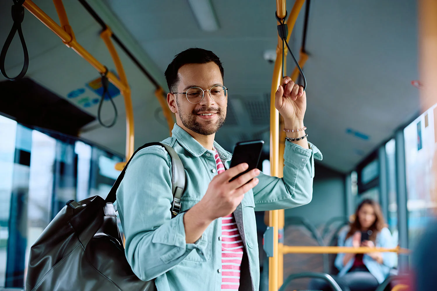 Ein Mann steht in der Straßenbahn und hält sich mit der linken Hand fest. In der rechten Hand hält er sein Handy