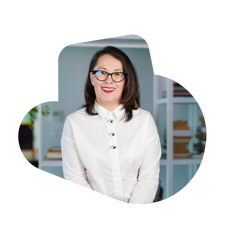 A brunette female engineer smiling at the camera, wearing a white blouse and black glasses