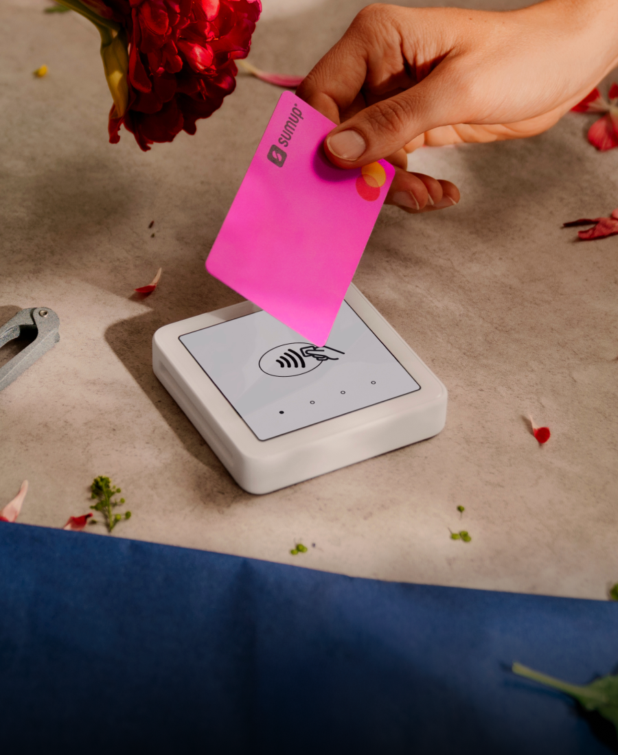 Iemand houdt een betaalpas tegen een SumUp-pinapparaat