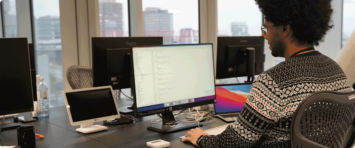 Male Android engineer working in front of a monitor showing a code and a laptop with a SumUp card reader and white POS device on the table.