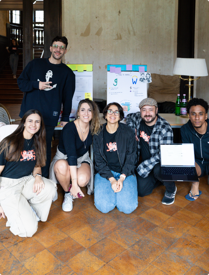 Group of six SumUp team members posing together indoors during Hack Week, with two project display boards and a laptop in front of them, all smiling and wearing Hack Week t-shirts or casual clothing.