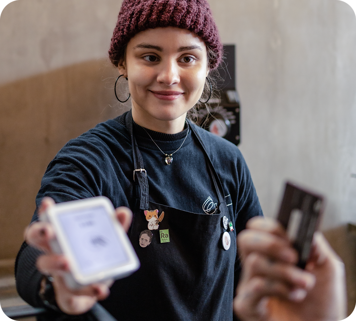 Barista smiling and holding a SumUp card reader toward the camera at a café counter.