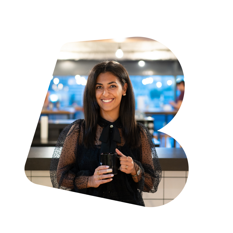 A female intern with black hair, holding a mug and wearing a black top in the kitchen of the SumUp Berlin office.