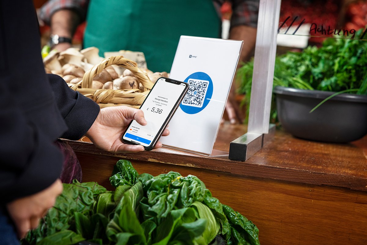 A customer holds their smartphone, about to complete a payment online after scanning a QR code display.