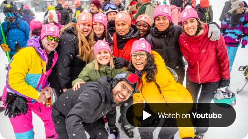 A mixed group of SumUppers wearing ski gear smiling at the camera, wearing branded pink SumUp beanies.