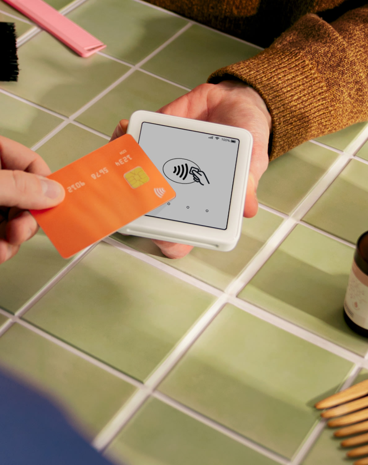 A person uses a contactless card on a SumUp Solo card reader, set on a tiled surface with various items in the background