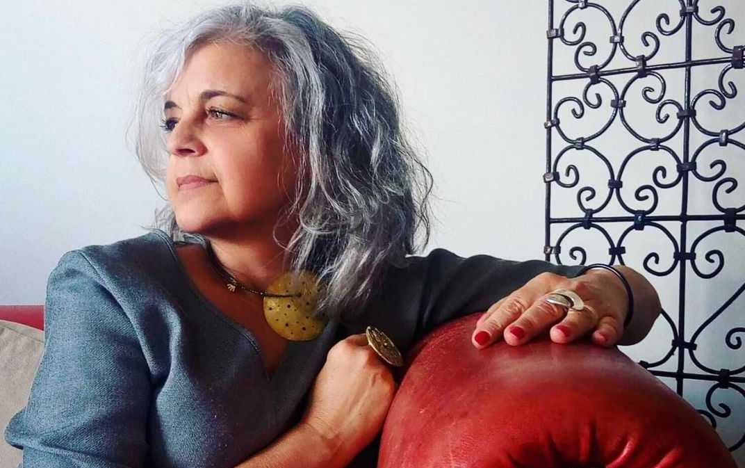 A woman sits on a sofa wearing accessories that she has handcrafted.