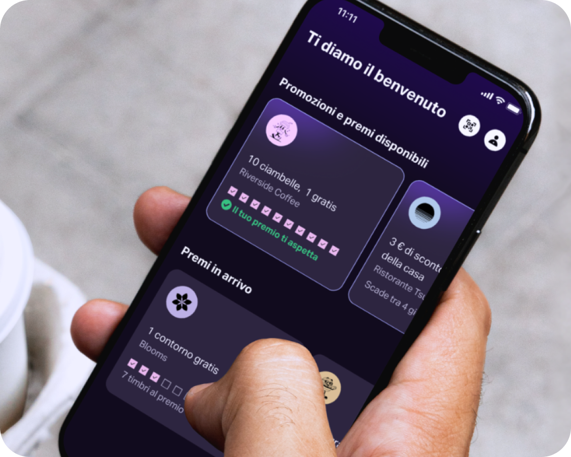 Una mano che tiene un cellulare con l'app SumUp Pay che mostra varie carte con programmi fedeltà.