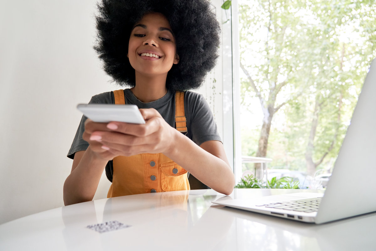 A young woman points her smartphone down at a QR code that is fixed to the table she is sitting at.