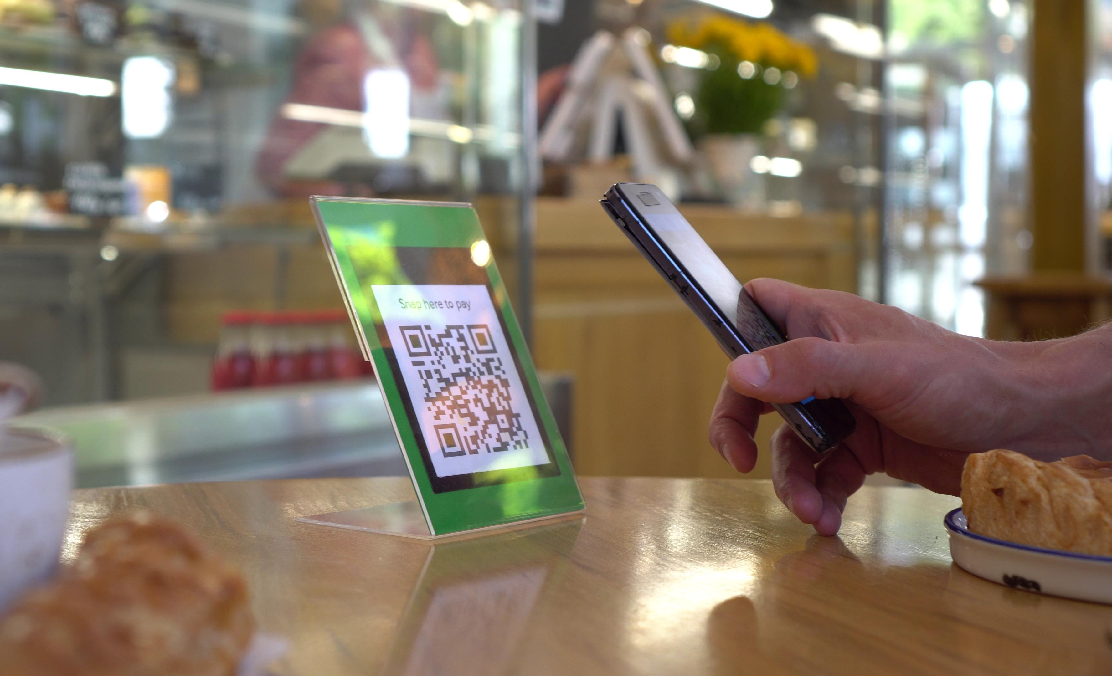 A customer uses their smartphone to scan a QR code at a table set with baked goods.