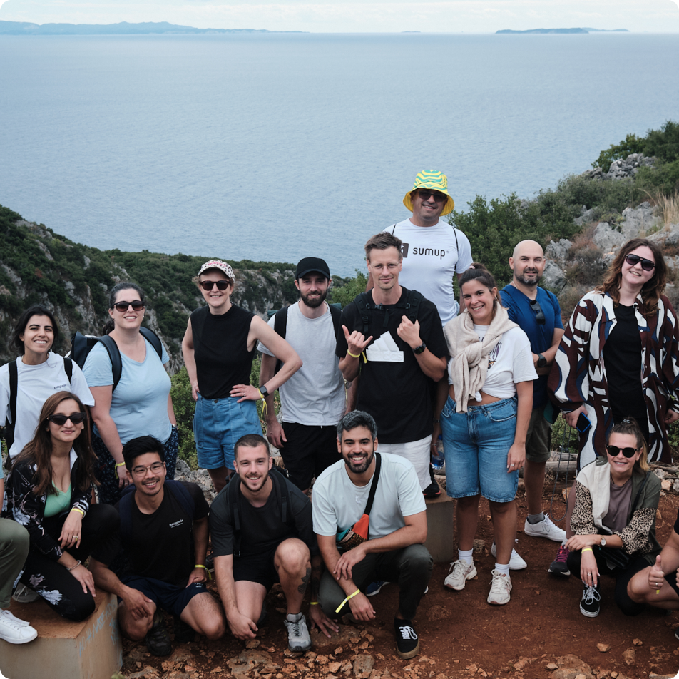 A group of SumUppers smiling together during an outdoor team activity with a scenic ocean view in the background.