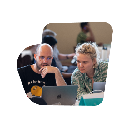 A female and a male SumUpper working together on a table using a laptop during Hack Week.