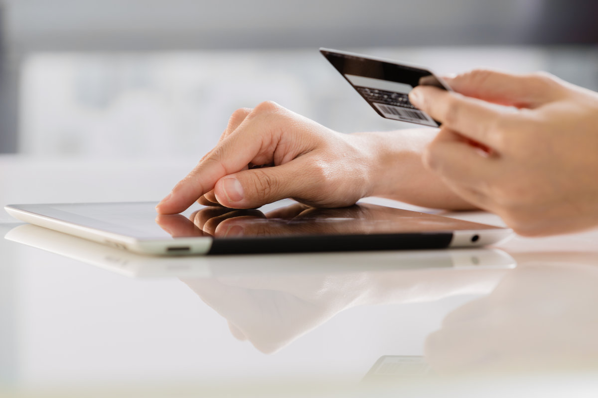 A person holding their credit card while they input their details on a tablet computer