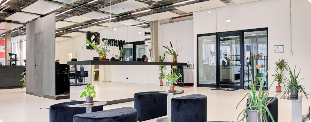Modern office reception area at SumUp with minimalist design, featuring black seating stools, potted plants, and glass doors. A mirrored wall displays the SumUp logo in the background.
