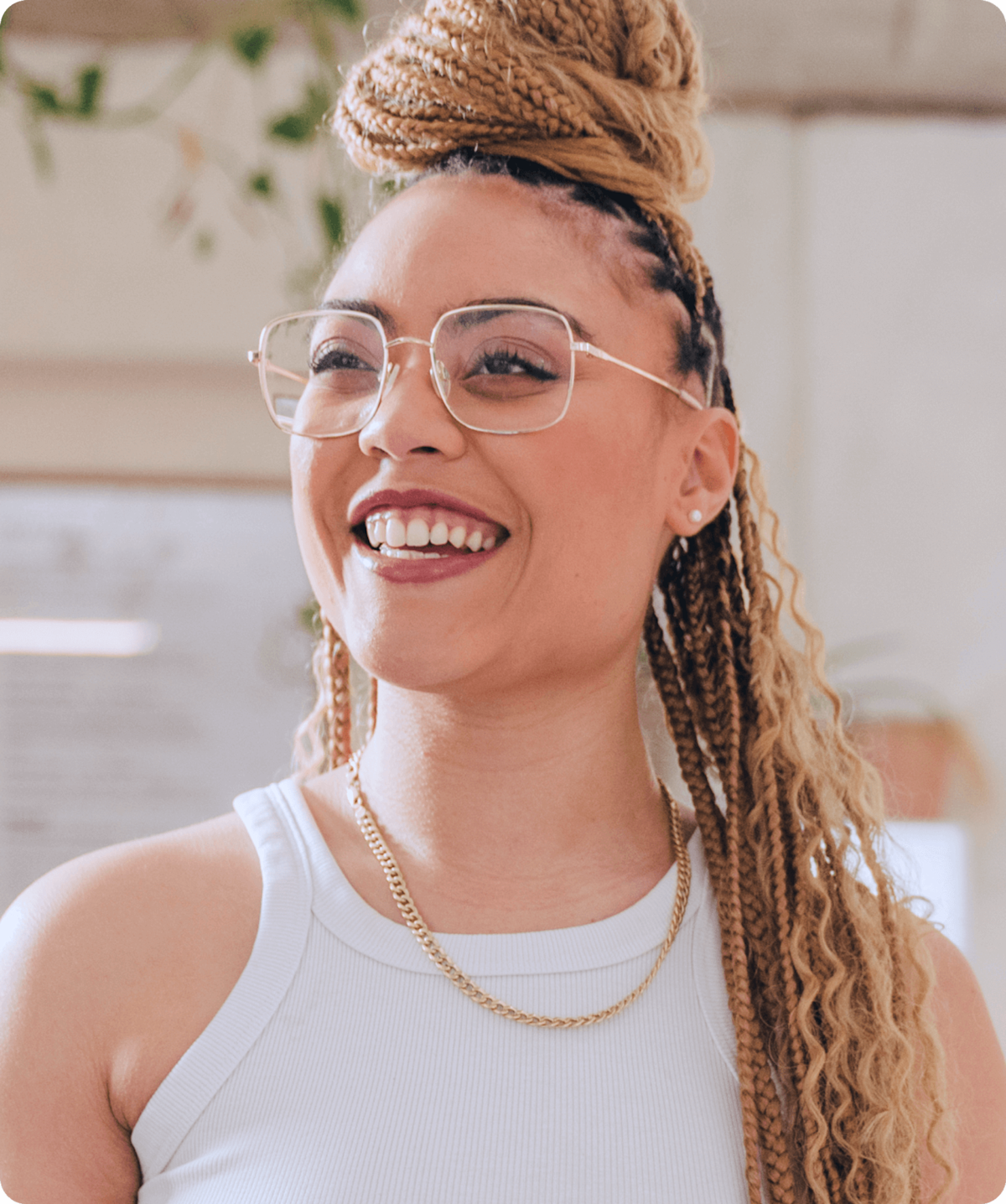 Smiling woman with glasses and braided hair in a top knot, wearing a white tank top and gold necklace.