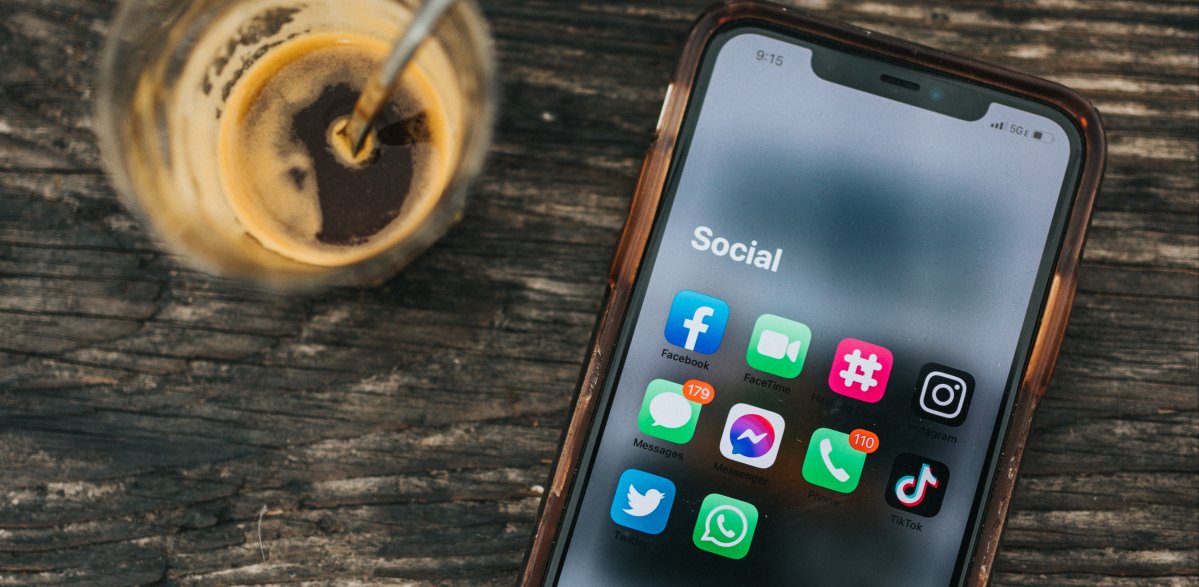 espressotasse und smartphone mit social media icons auf einem holztisch