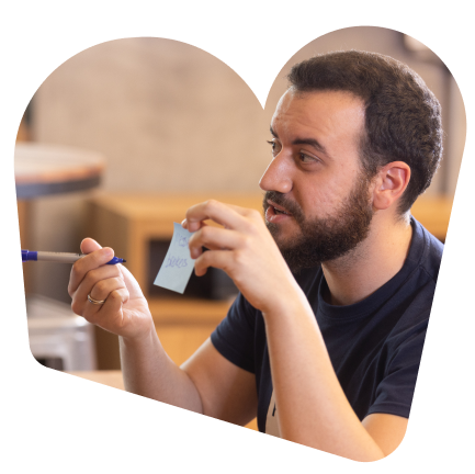 A male SumUpper with short brown hair holding a blue sticky note and a pen.