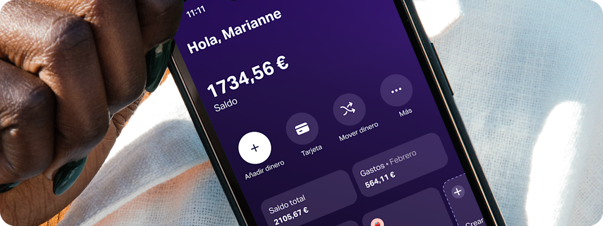 Primer plano de una mano sujetando un smartphone que muestra la aplicación SumUp Pay; en ella se ve un espacio de ahorro para "Viaje por carretera".