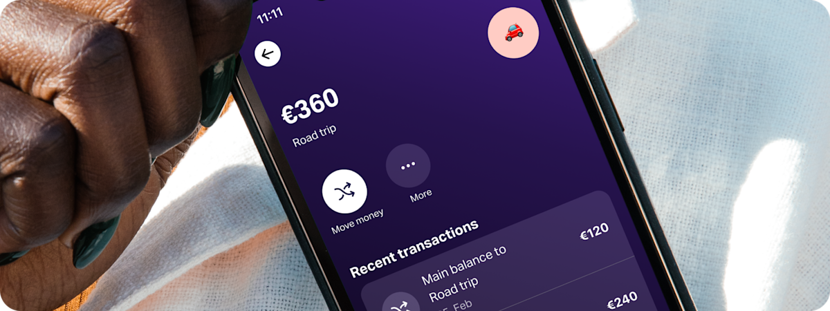 Close-up of a hand holding a smartphone displaying the SumUp Pay app, showing a ‘Road trip’ savings space.