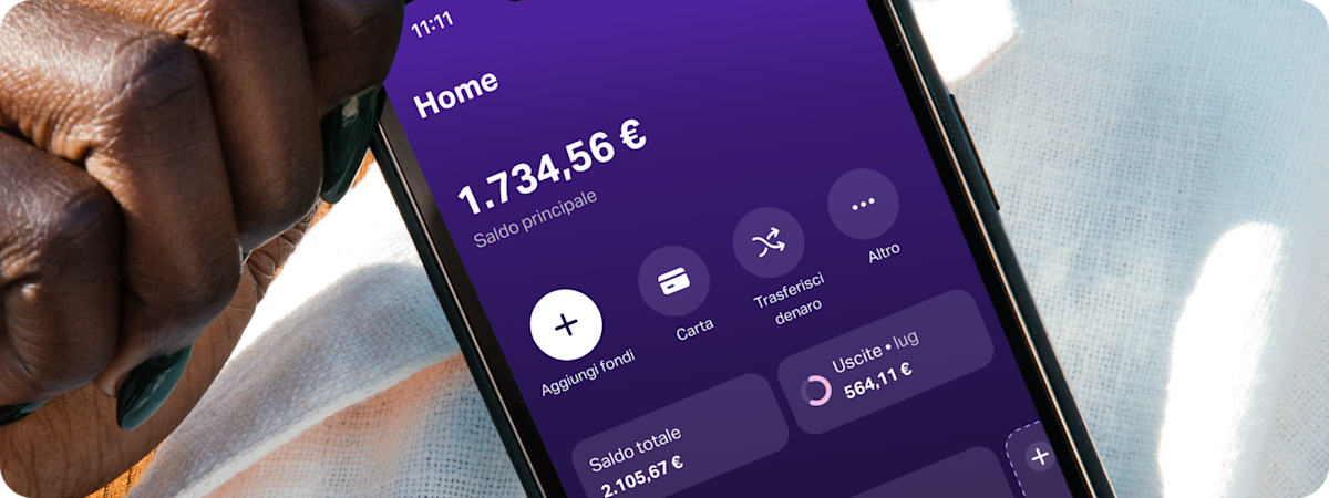 Primo piano di una mano che tiene uno smartphone sui cui è visibile l'app SumUp Pay, che mostra un'area risparmi chiamata "Viaggio".