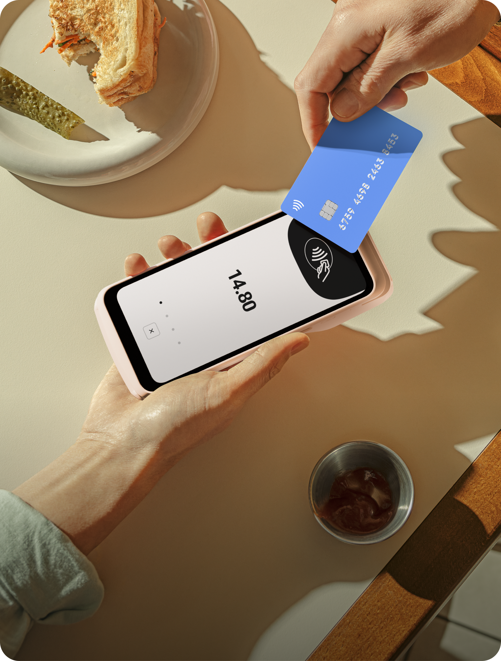 SumUp payment terminal sits on a wooden surface displaying a contactless payment symbol. Nearby, a spool of twine and green plant provide context.