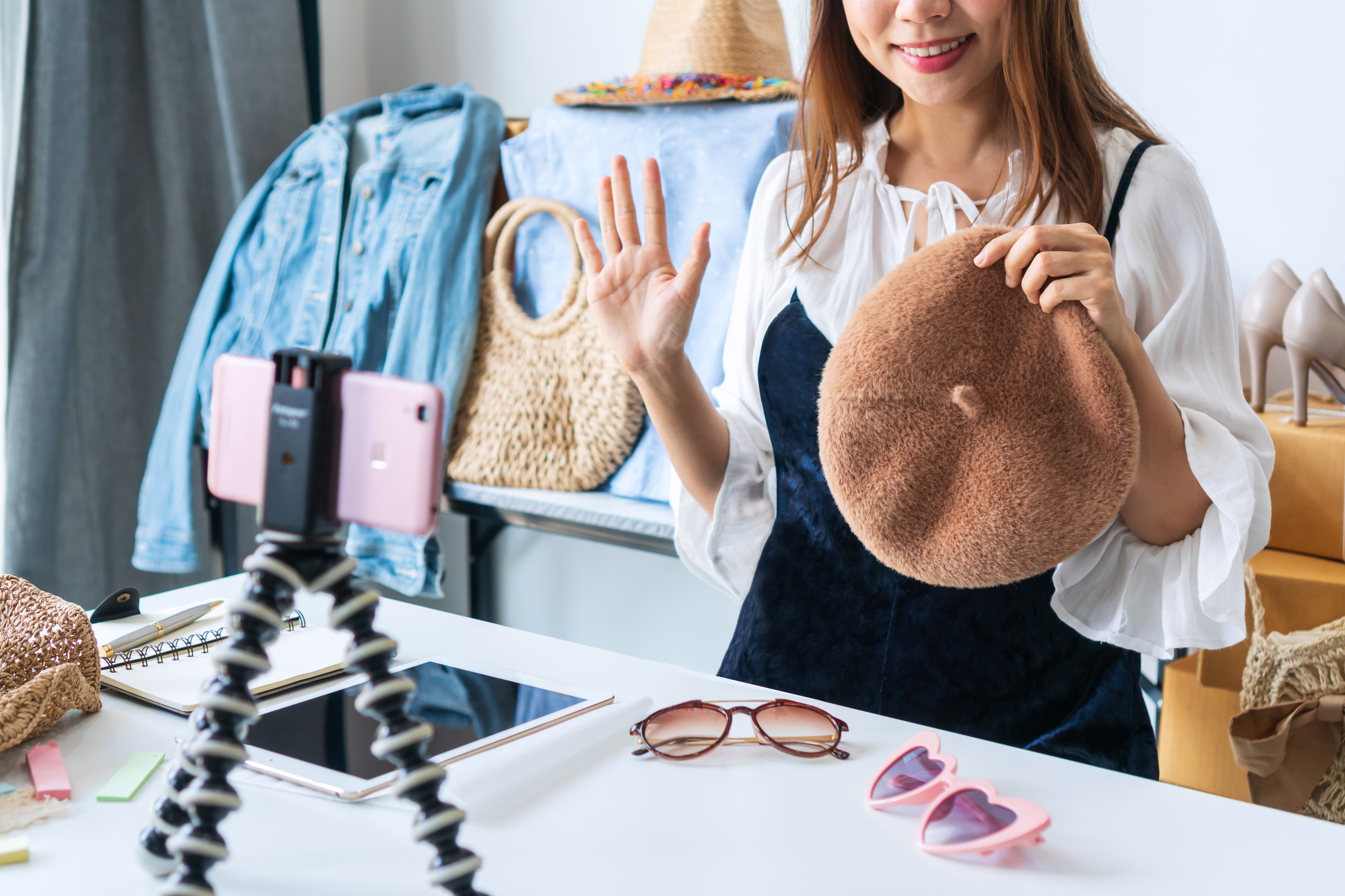 A woman holding up an item of clothing while surrounded by other clothes.