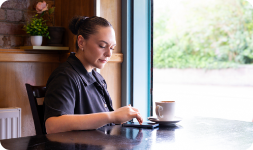 Female Field Sales Consultant using a smartphone in a café, connecting with small business owners as part of SumUp’s UK sales team.