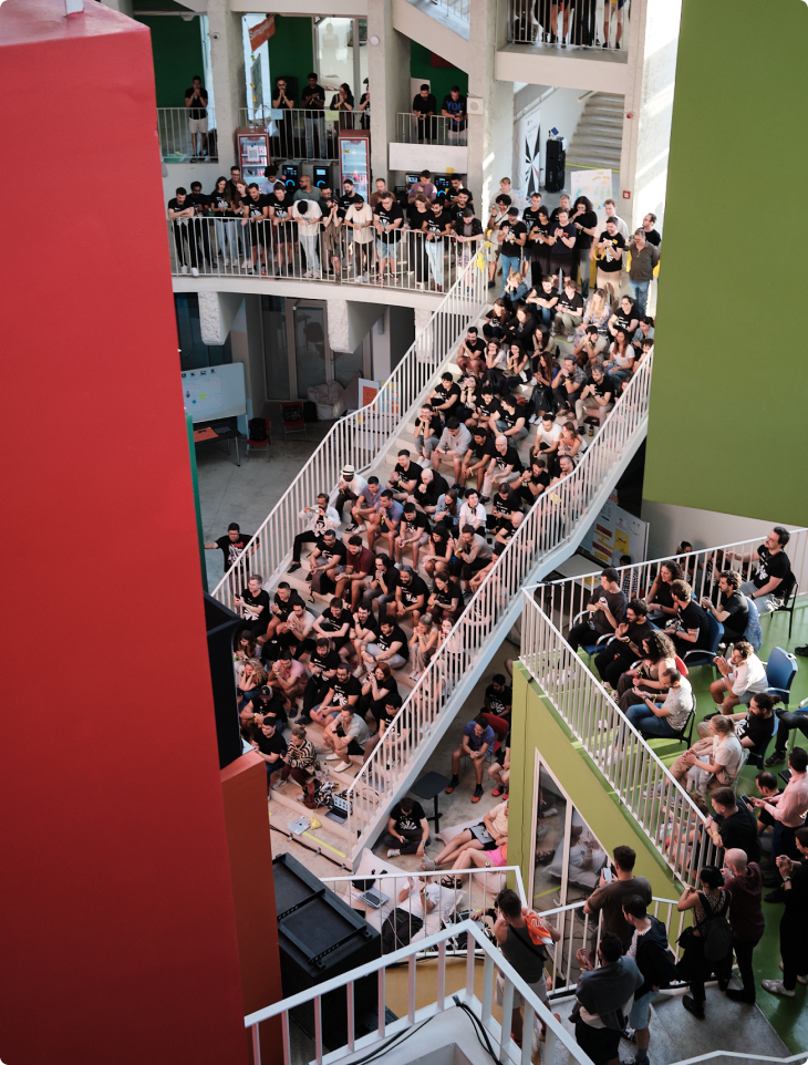 A large group of SumUp team members gathered on tiered seating and balconies inside the Pyramid of Tirana during Hack Week 2024, listening to a presentation in a bright, colourful space.