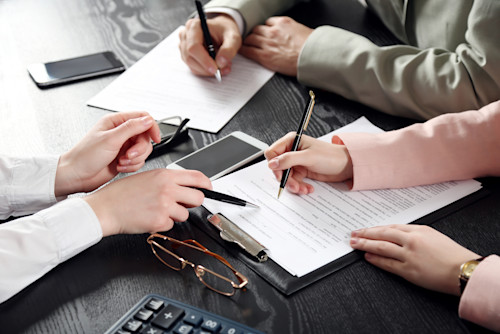three people signing paperwork on a desk