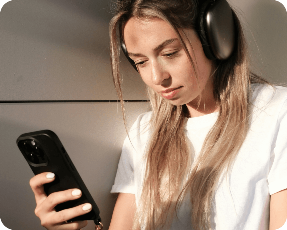 Photo of a woman wearing headphones looking at her mobile phone.