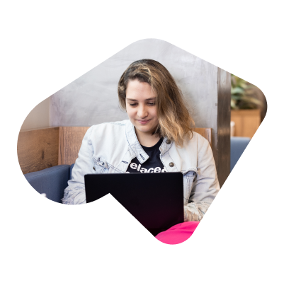 A young female engineer working on a black laptop, wearing a black denim jacket, a black t-shirt and pink pants.