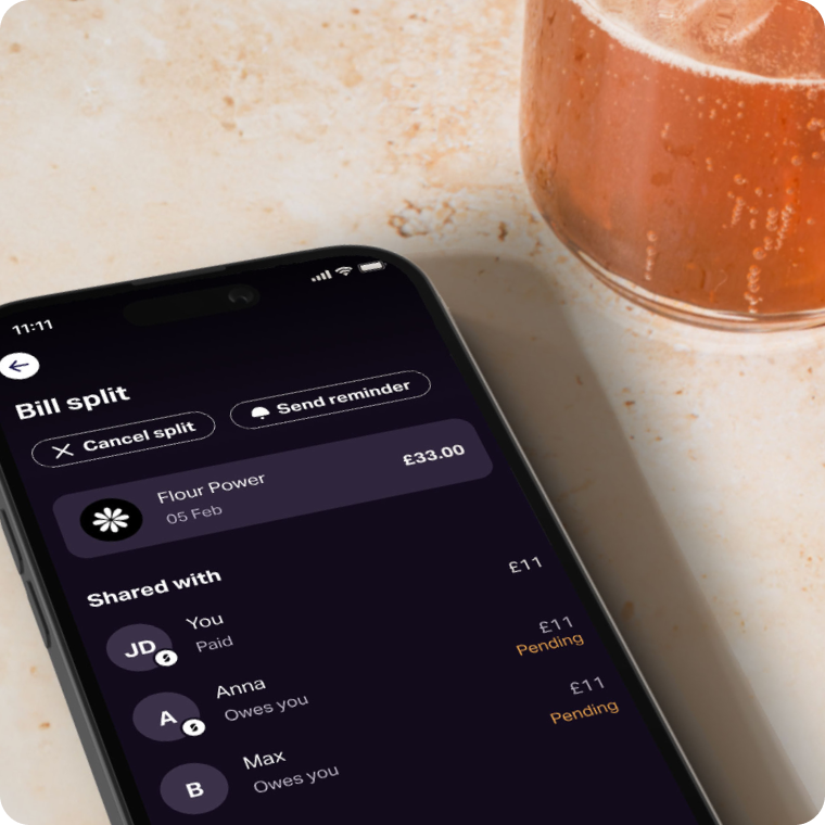 Smartphone on a café table shows SumUp Pay bill-split screen for a £33 Flour Power expense shared with friends, with cancel and reminder buttons; a glass of beer sits nearby.