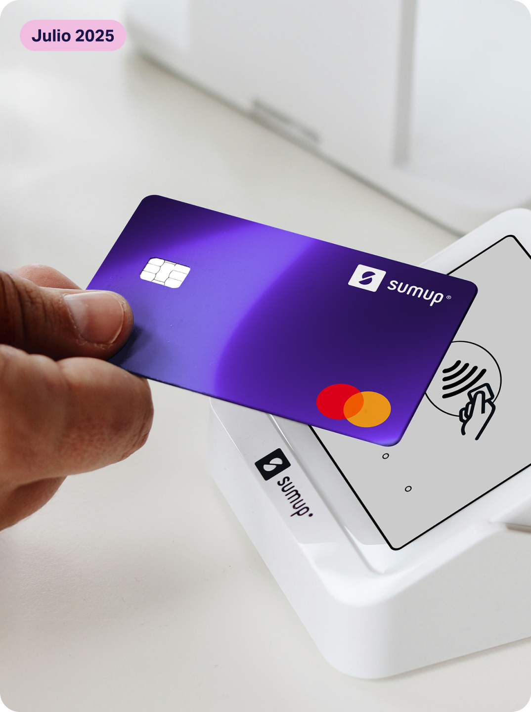 Una persona acerca una tarjeta de débito física de SumUp Pay a un datáfono SumUp para hacer un pago contactless. Etiqueta rosa "próximamente" en la parte superior izquierda.