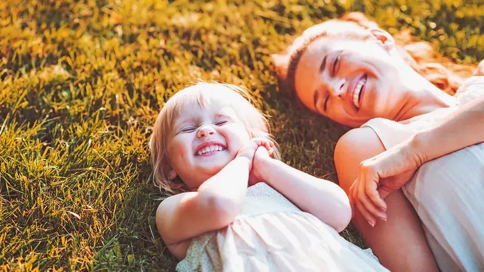 A young girl and a woman laughing in the grass.