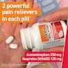 A hand holds a bottle of Motrin Dual Action with Tylenol. Two white, oval-shaped pills are visible in the foreground.