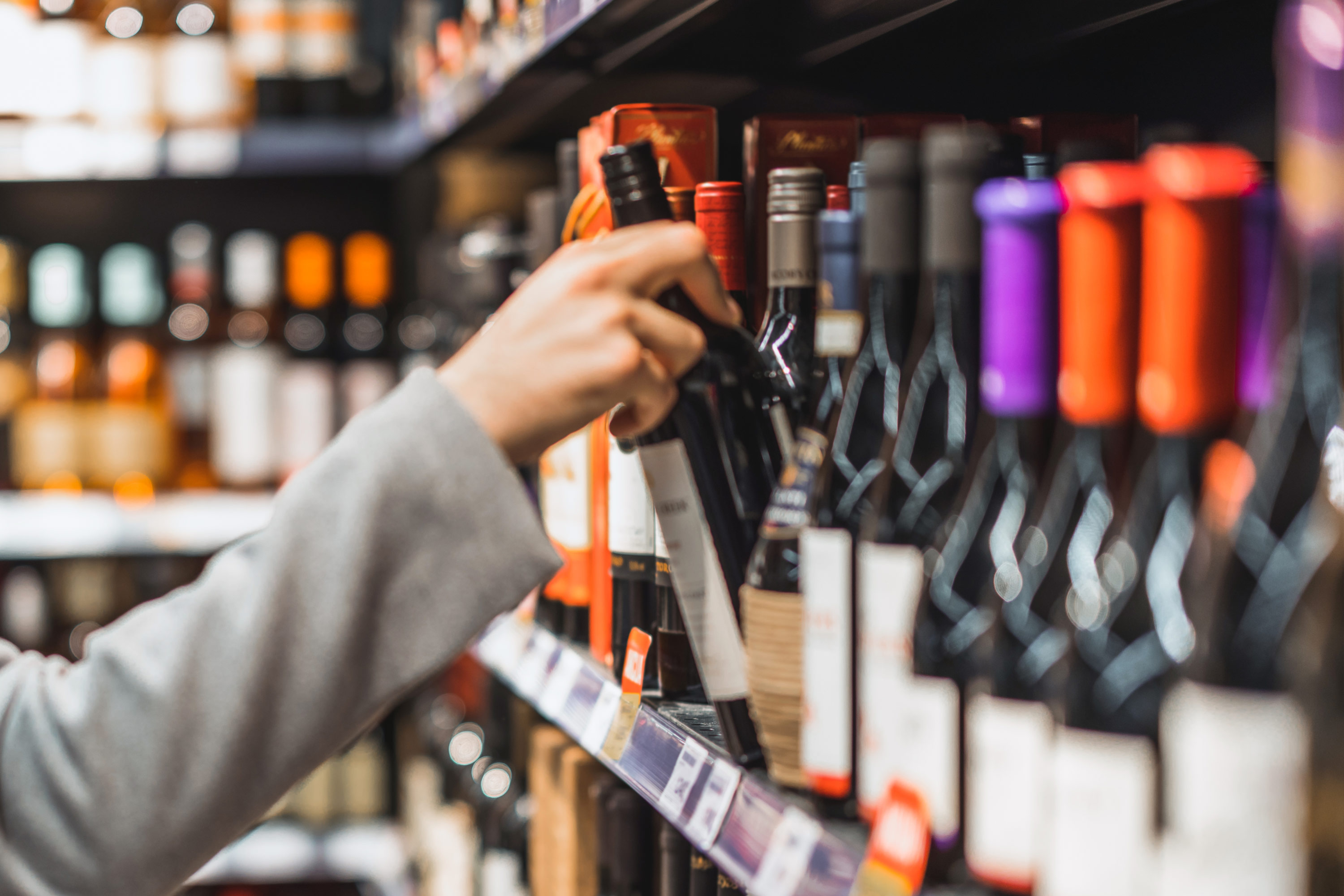 A person taking a bottle of alcohol off the shelf.