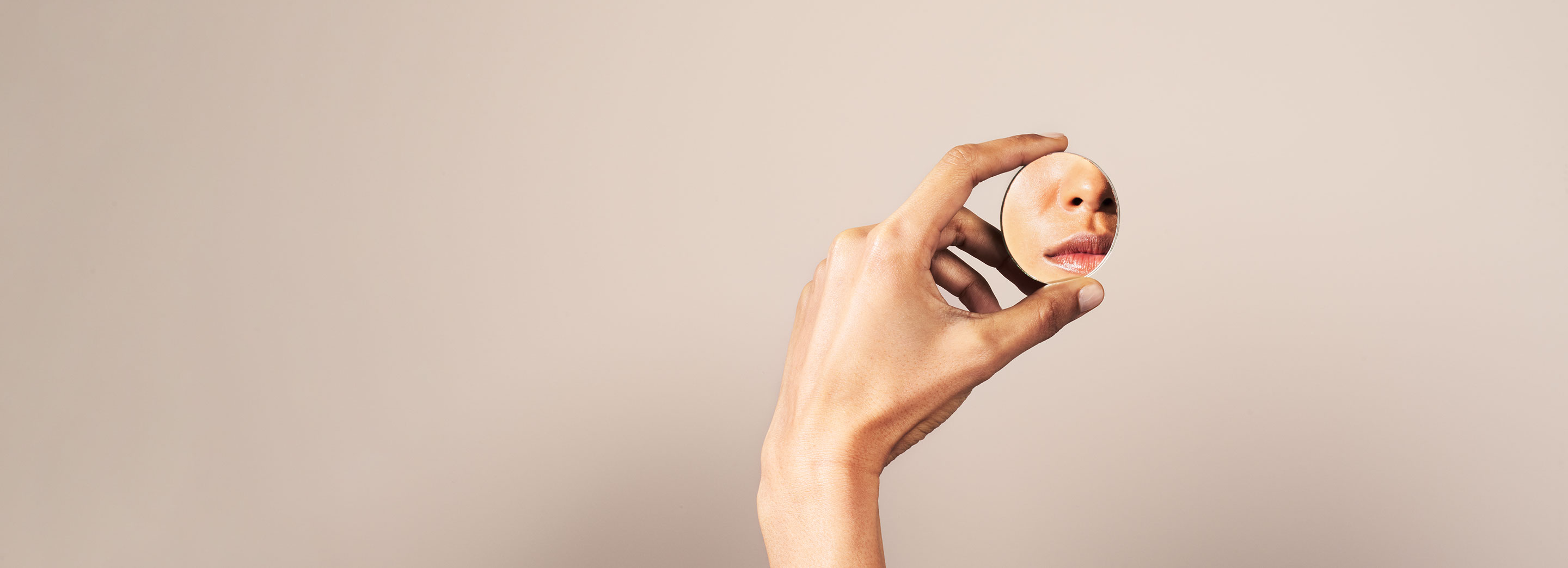 hand holding a round mirror in dusty pink background