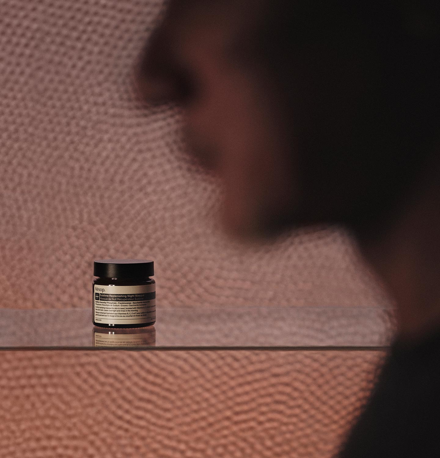A jar of Sublime Replenishing Night Masque sitting in front of a textured glass window.