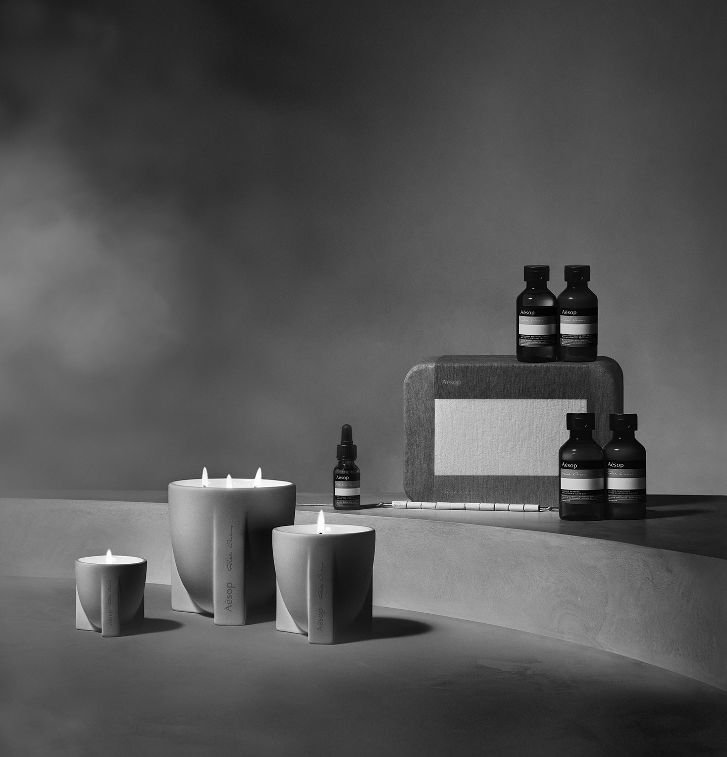 Aesop Rick Owen Travel Kit and Stoic Aromatique Candles sitting on a concrete surface.