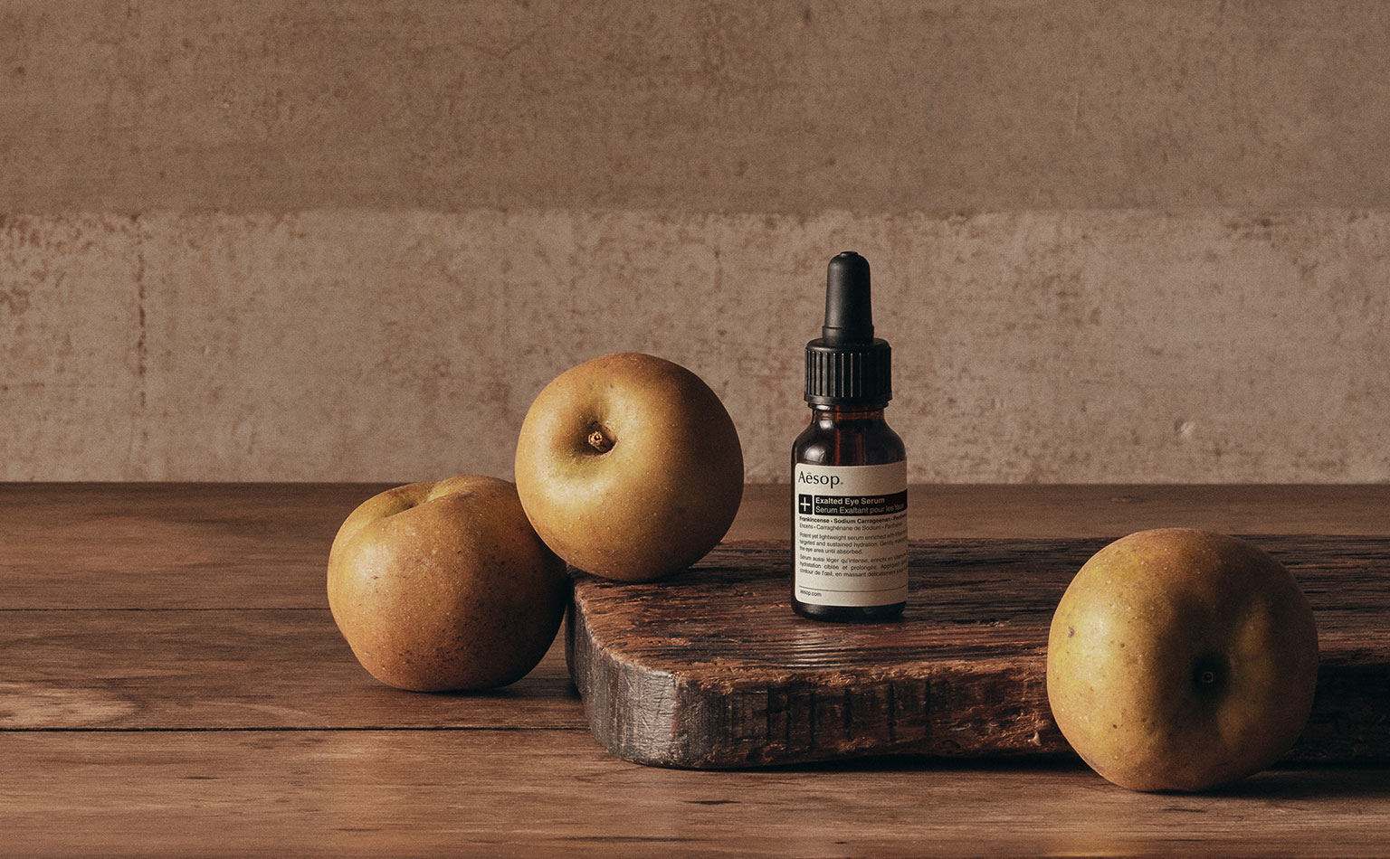 Bottle of Exalted Eye Serum sitting alongside fruit on a wooden surface.