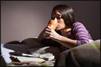 Photo of young lady drinking beverage at night in bed.