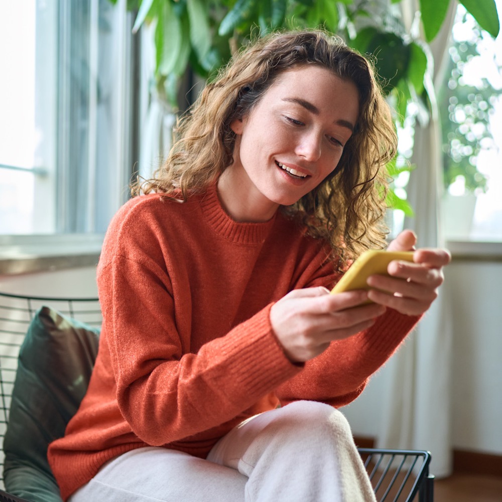 woman in orange sweater holding a cell phone - from shutterstock