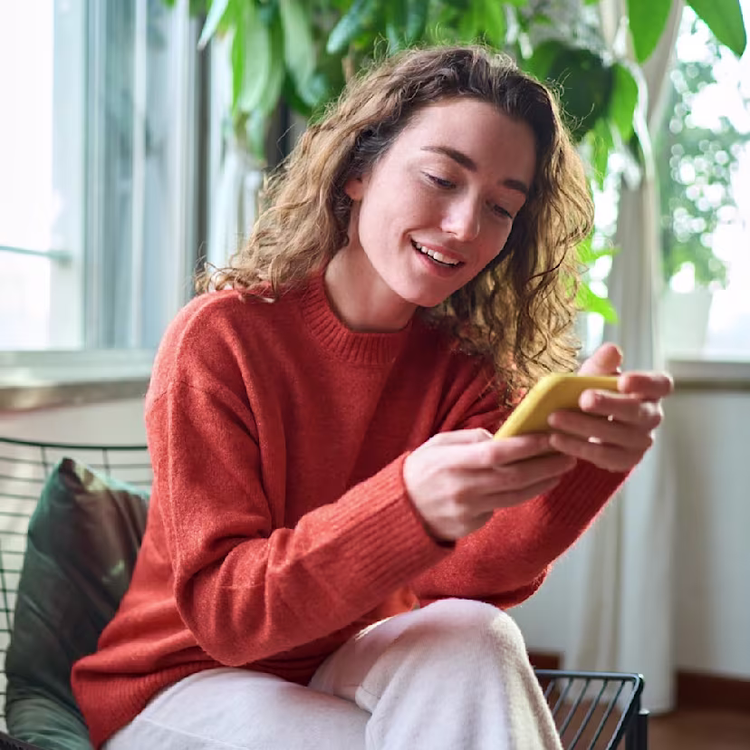 woman in orange sweater holding a cell phone - from shutterstock