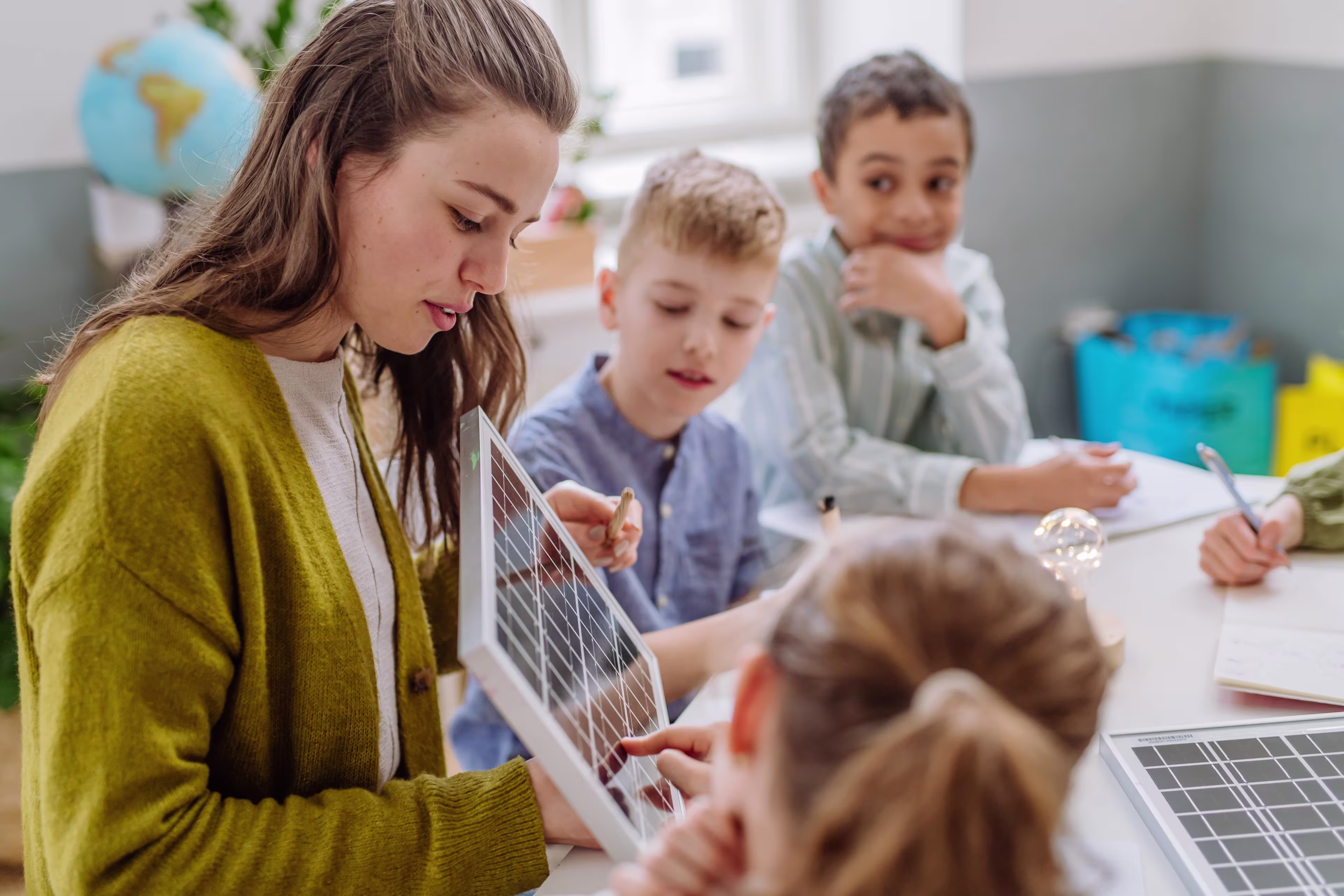 Woman teaching a group of children, pointing to a board.