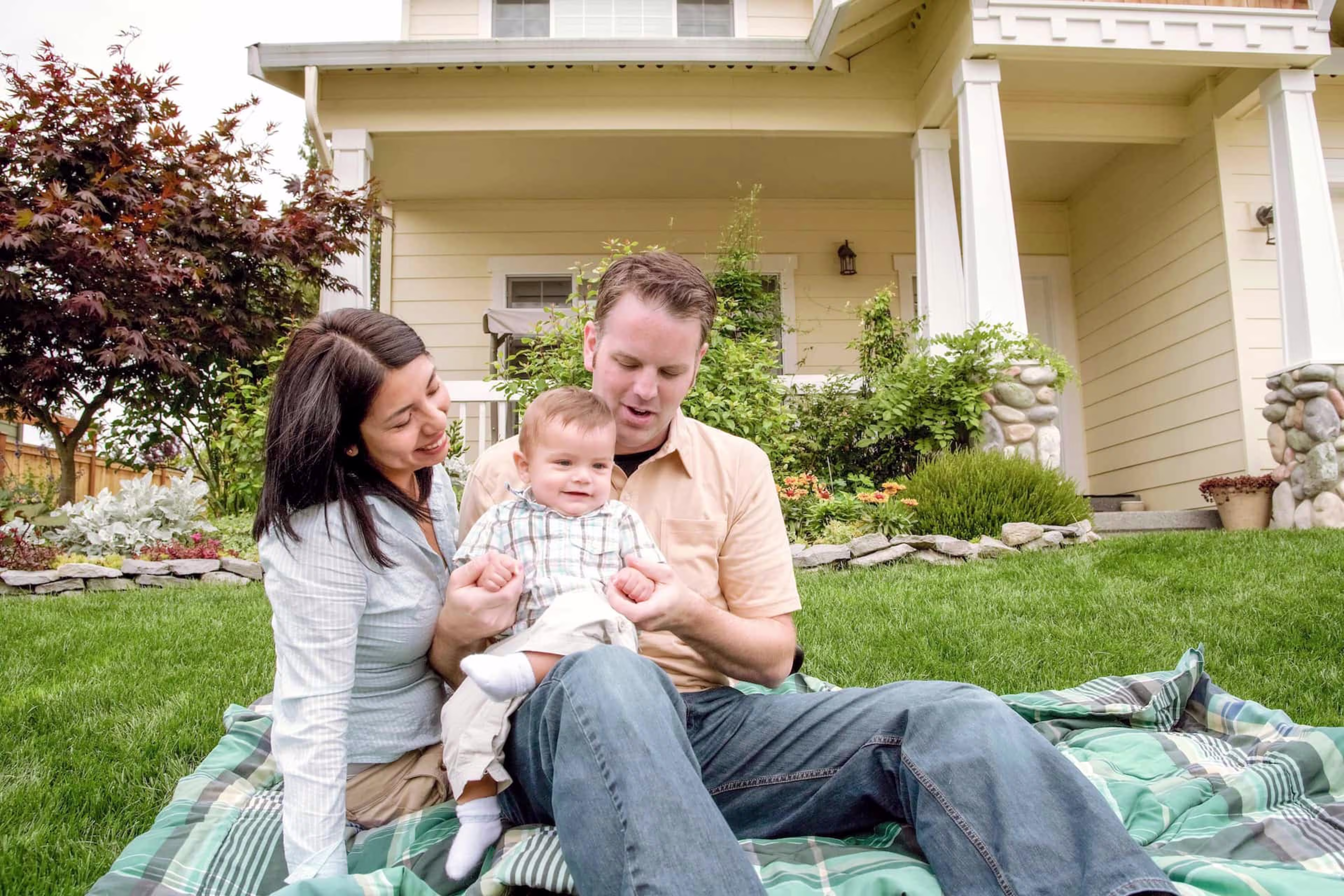 Family with a baby on a picnic blanket in front of a house