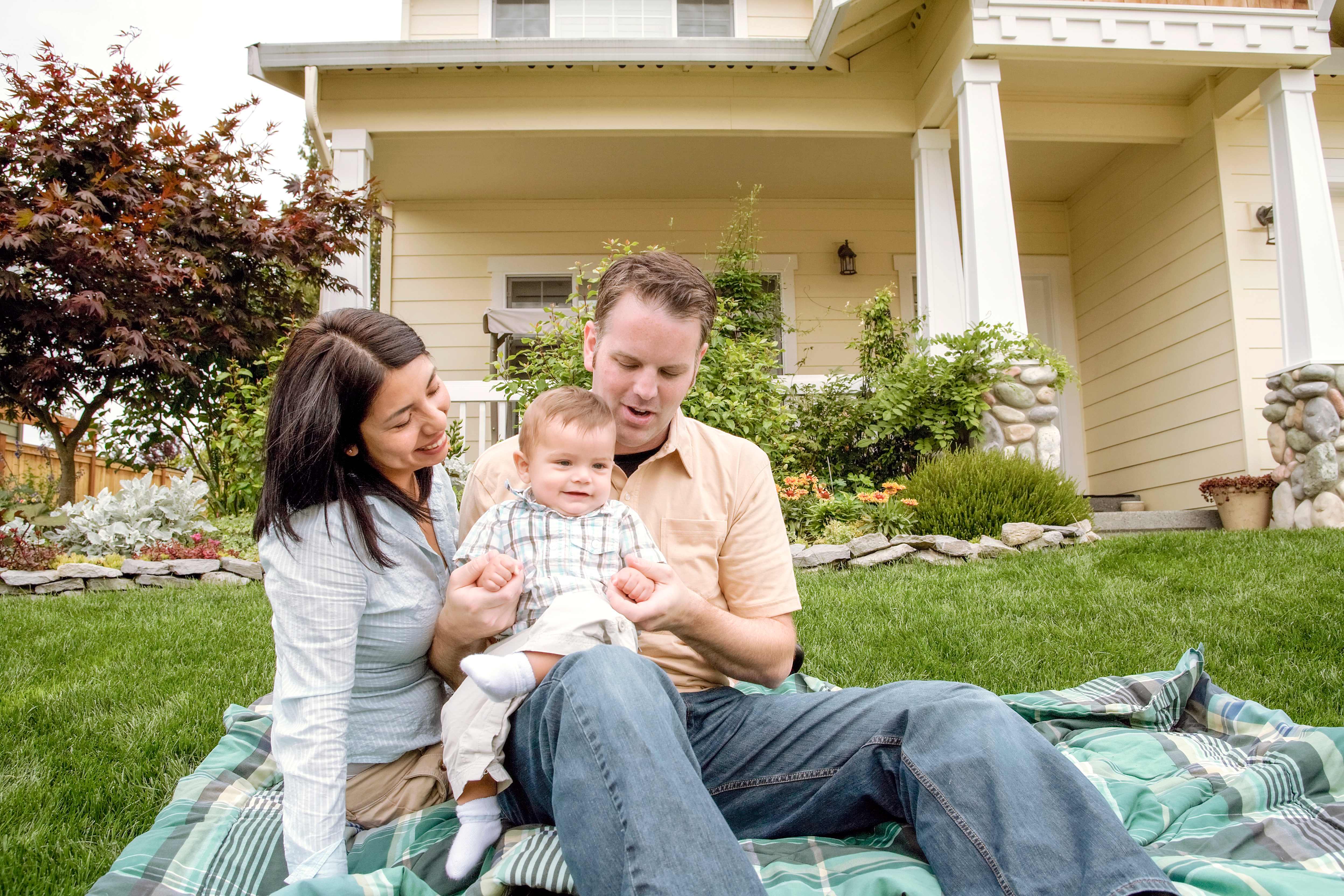 Family with a baby on a picnic blanket in front of a house