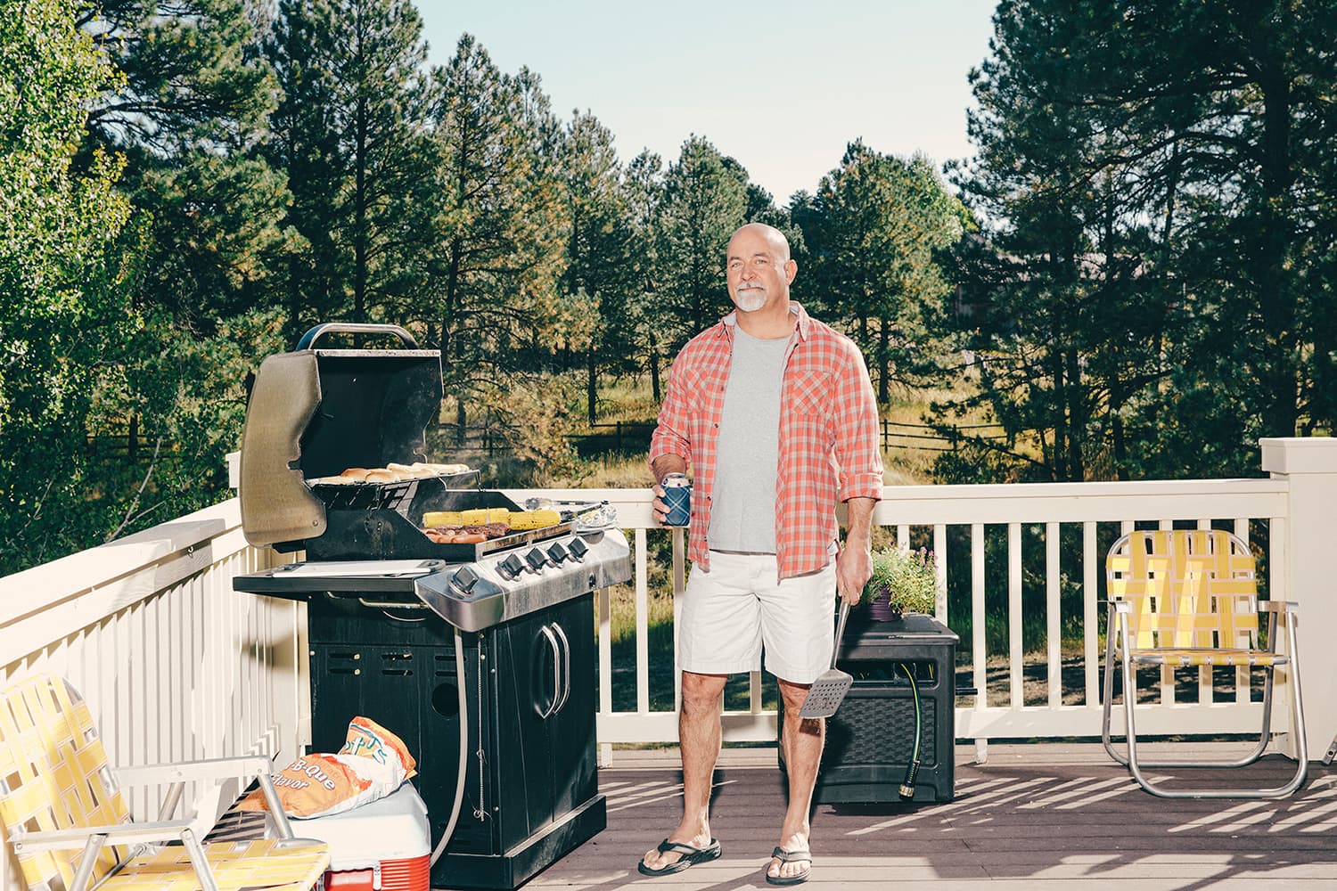Man standing next to his grill on his deck, holding a beverage