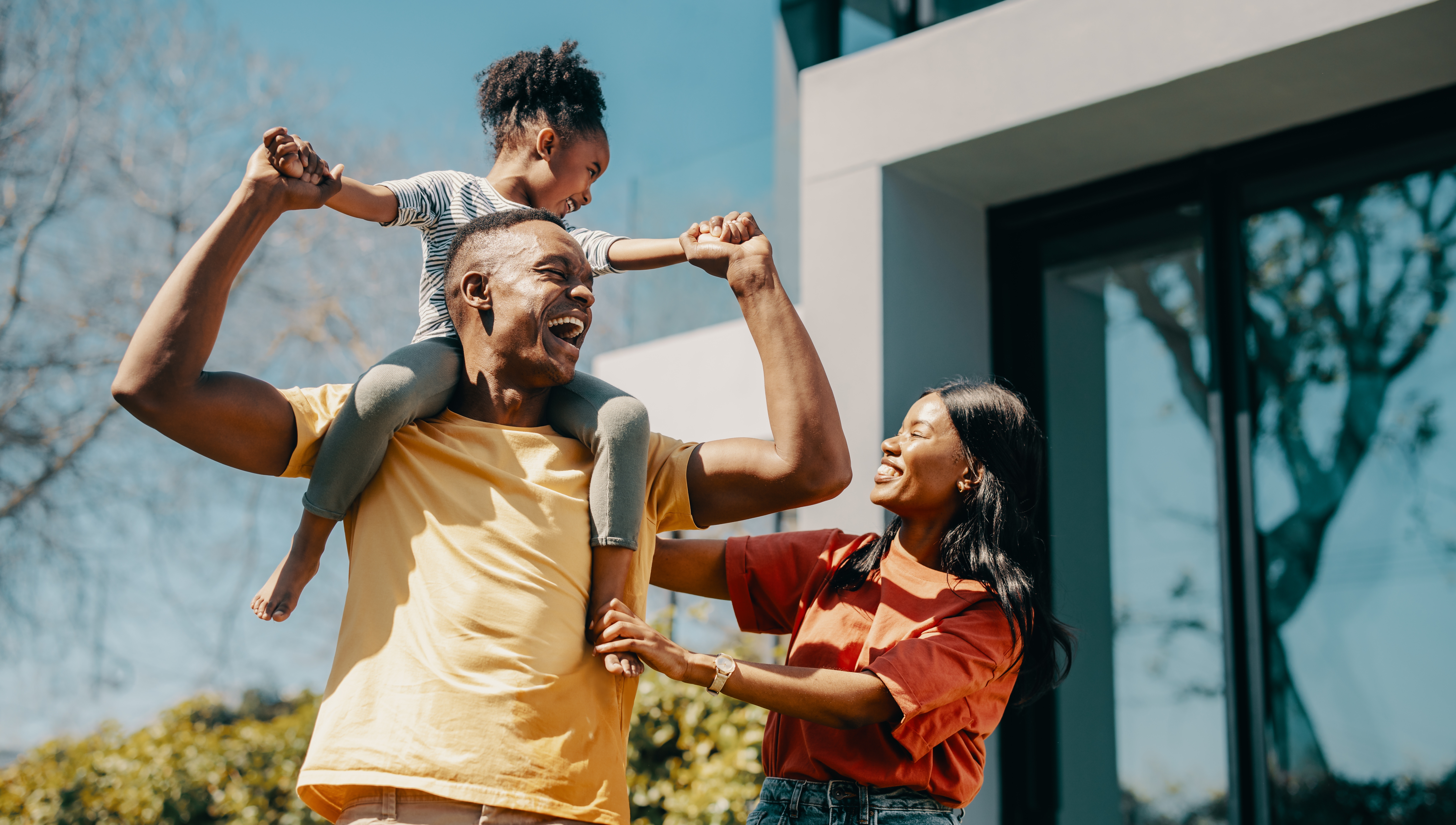 Mom and Dad with child on shoulders in front of a house